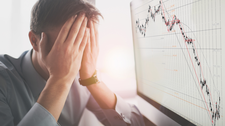 A man is sitting with his face in his hands next to a chart with a plot line that is steeply trending downwards.