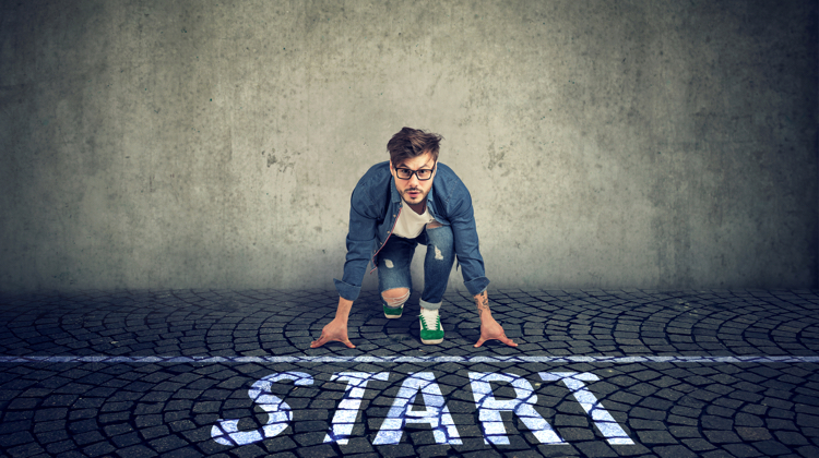 Man in jeans and sneakers with a denim top squats on cobblestones in front of a line that says START