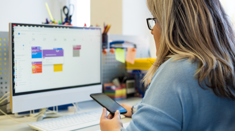 A woman sitting at her desk looking at a digital calendar on her computer.