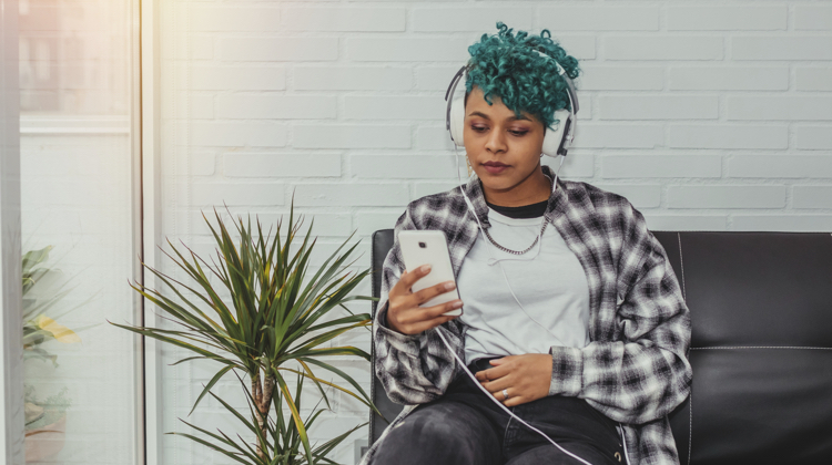 A woman sitting on a couch listening to something through headphones.