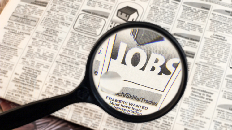 A magnifying glass is hovering over the classified section of a newspaper and through the lense there is a section of the paper that reads "jobs".