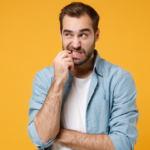 Man stands against a bright yellow background, biting his finger in a look of confusion.