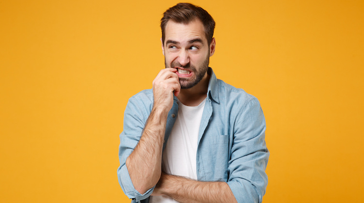 Man stands against a bright yellow background, biting his finger in a look of confusion.