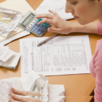 Woman looking down at papers on a desk and calculating figures on a calculator