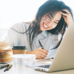 Smiling woman writing in tablet in front of a laptop with a coffee at her side