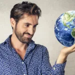 Bearded man in patterned blue dress shirt holds a globe