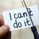 Left hand holds a small white paper with the words "I can't do it" and the right hand has scissors cutting through it.