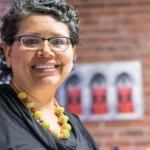 Smiling woman wearing glasses and chunky yellow necklace and black dress shirt