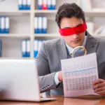 A man sitting blindfolded at a desk.