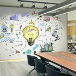 An office conference room is show with a wooden desk and black plastic chairs in front of a whiteboard with graphics