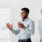 Man in long-sleeved, button-down shirt stands in front of a paper presentation