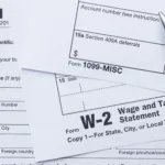 W-2 and 1099 tax forms with a pen resting on top; the #1 tax mistake freelancers make is not saving enough