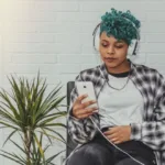 A woman sitting on a couch listening to something through headphones.