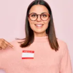 woman smiling pointing at a blank name tag on her chest