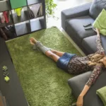 woman with her eyes closed lying on floor in front of a couch, arms akimbo with pillows strewn around her