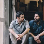 Two men sitting on a stoop with crossed hands deep in conversation