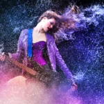 Woman on black background with guitar flips hair back, making it look like she's surrounded by a field of glitter