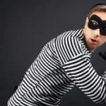 Man in white and black striped shirt and black mask looks behind his back as he prepares to run away