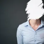 Woman in blue, button-up shirt against black background with her face scratched out