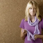 Blonde woman wearing a purple shirt and scarf looks anxious as she bites her lip