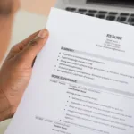 Hands hold a printed resume in front of laptop keys.