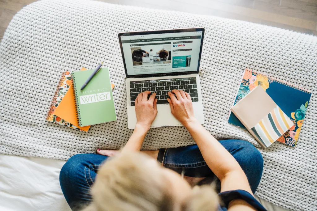 Nicki Krawczyk, founder of Filthy Rich Writer, types on a laptop with notebooks on either side.