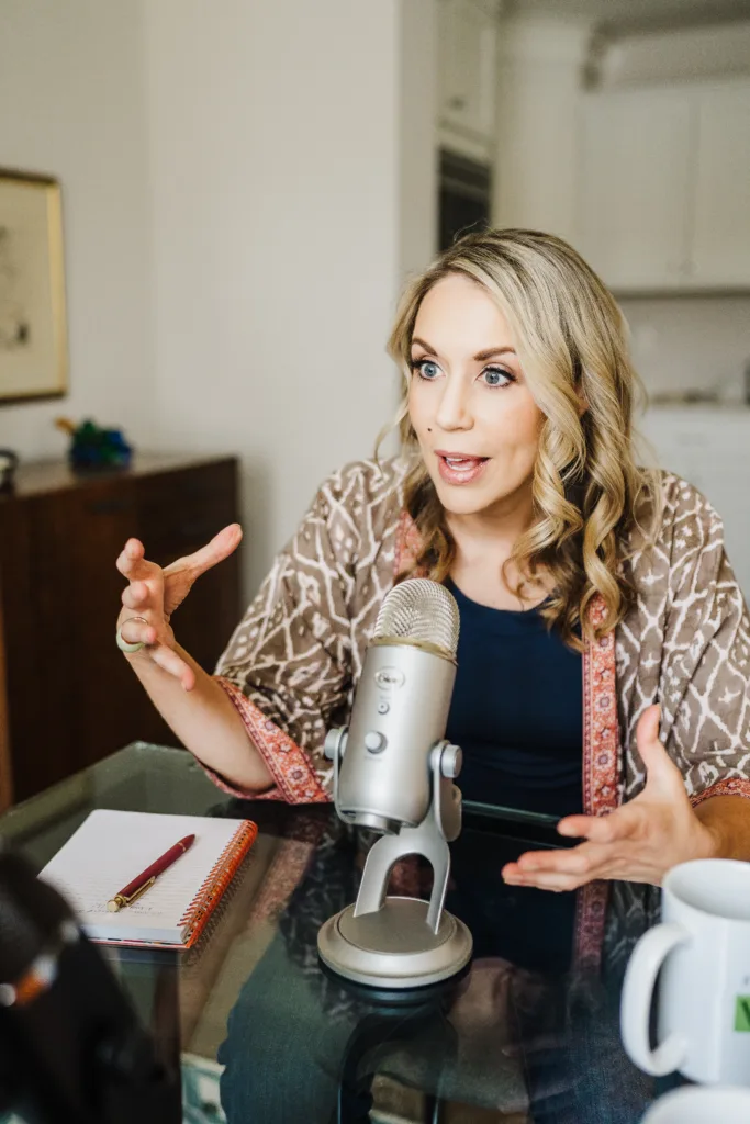 Nicki Krawczyk, host of the Build Your Copywriting Business podcast, sits at a desk and speaks into a microphone.