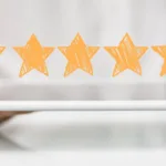 Hand holds a white tablet with five yellow stars hovering above it.