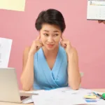 Woman at desk with laptop and papers blocking ears as a bunch of hands compete for her attention