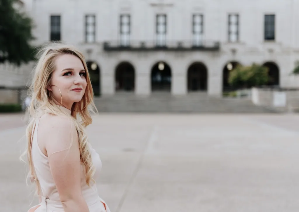 CCA student Shelby stands outside in a white dress with her head turned to the camera