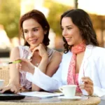 Two women reviewing work on a laptop while having coffee