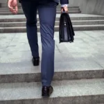 View of a grey staircase where legs in a blue suit and an arm holding a black briefcase walk up the steps.