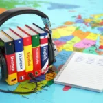 Set of dictionaries in different languages with headphones surrounding them sitting on a map of the world next to a notebook of words