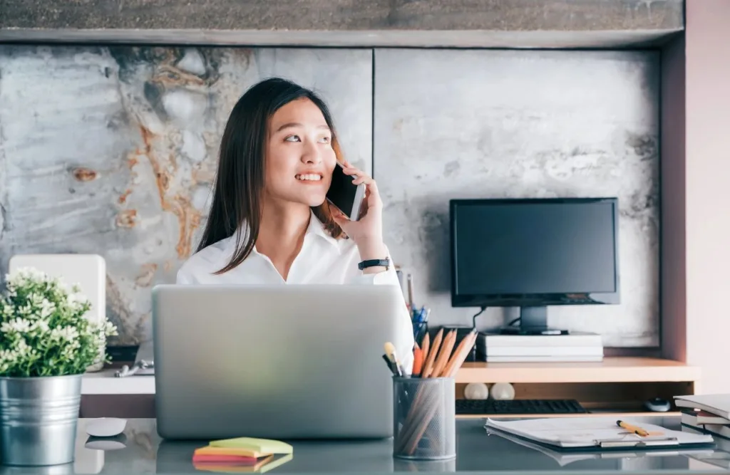 Woman on phone in front of laptop in a home office