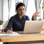 Young woman sits in front of laptop with headphones on a remote call of laptop on